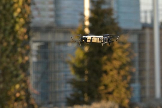 Handtellergrosse graue Drohne im Flug vor dunklem Hintergrund.